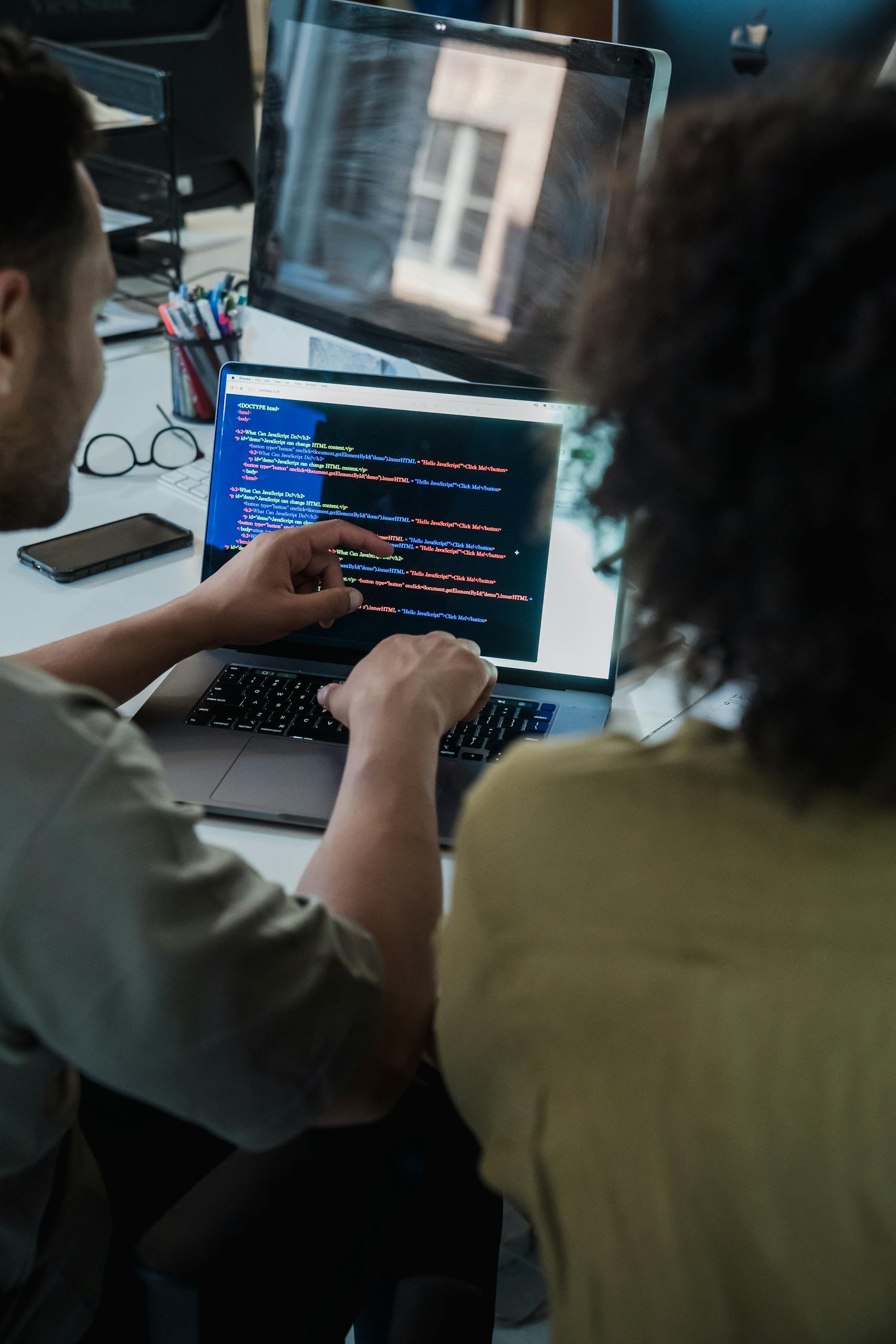 Two adults collaborating on programming tasks using a laptop in an office setting.